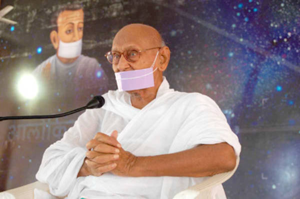 The previous head of the Śvetāmbara Terāpanthin sect, Ācārya Mahāprajña preaches to followers. Behind him is a background with a picture of the founder of the sect, Ācārya Bhikṣu