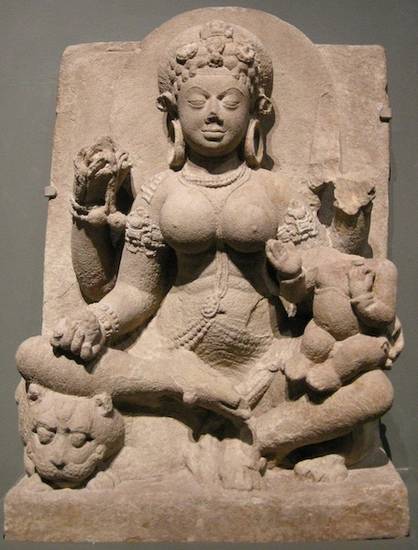 Sandstone sculpture of the goddess Ambikā sitting on her divine vehicle of a lion, holds her divine attribute of mangoes in one of her four hands. Another hand rests protectively on the damaged figure of a small child on her knee.