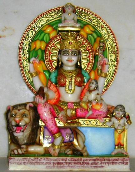 The popular goddess Ambikā as a colourful Śvetāmbara image. Her divine vehicle of a lion and her divine attributes of mangoes and children are clearly visible. A small figure of the 22nd Jina Nemi, to whom Ambikā is the yakṣī, is above her head.