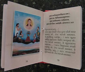 Pages of a miniature edition of the Bhaktāmara-stotra, showing verse 26 facing a modern illustration. The original Sanskrit is given in Devanāgarī script, with Gujarati translation in Gujarati script below. The picture shows a scene of homage