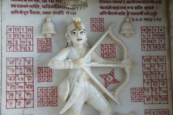 Ghaṇṭākarṇa Mahāvīra in a temple in Jaipur. Above the protective deity is his Sanskrit mantra, with the squares of numbers at the sides indicating how many times it should be recited. On each side of his head are two bells, as his name means 'Bell-ears'