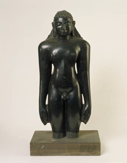 Part of the stone figure of a Jina carved in typical Digambara style. This tenth-century idol from southern India portrays a Jina in the kāyotsarga pose. This standing posture involves such deep meditation that one is unaware of the physical world.