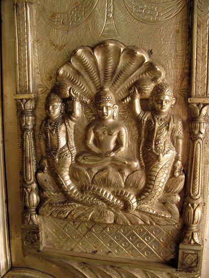 Pārśvanātha or Lord Pārśva sits in the lotus pose commonly used for Jinas. Above his head five serpent heads fan out while his half-snake attendant gods stand either side. The yakṣas hold fly-whisks, which, along with his jewellery, underline his status.t