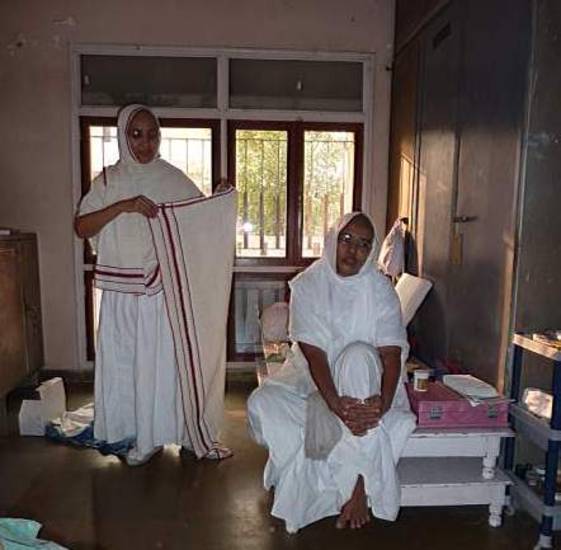 Two Śvetāmbara nuns inside their lodgings – upāśraya. One wears the full nun's outfit, ready to begin the alms-round. Strict rules specify that nuns must wear white robes that completely cover them while in public