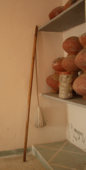 The monastic staff and broom of a Śvetāmbara mendicant lean against shelves in a corner. Monks and nuns in the Śvetāmbara sect use alms bowls, staffs and brooms as their monastic equipment – upakaraṇa