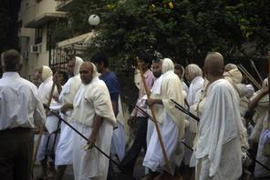 Śvetāmbara monks walk down a Mumbai street accompanied by lay men. The monks are barefoot and holding their mouth-cloths and monastic staffs. Jain mendicants live in small bands and travel most of the year in the traditional wandering lifestyle – vihāra