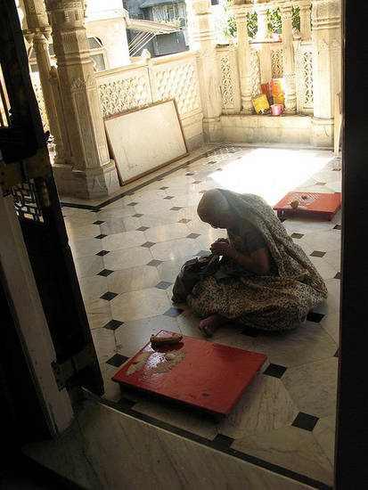 A lay woman prepares to make auspicious symbols in the temple. She will use the rice grains, banana and half an egg to create patterns on the red board. Behind her is a tray with some finished symbols.