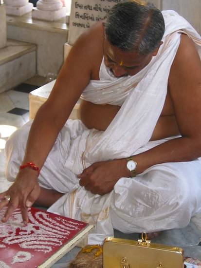 A lay man makes auspicious symbols in uncooked rice in a temple in Mumbai. Creating auspicious symbols such as the svastika or auṃ mantra is one of the rituals of Jain prayer, which revolves around making offerings and singing or chanting hymns.