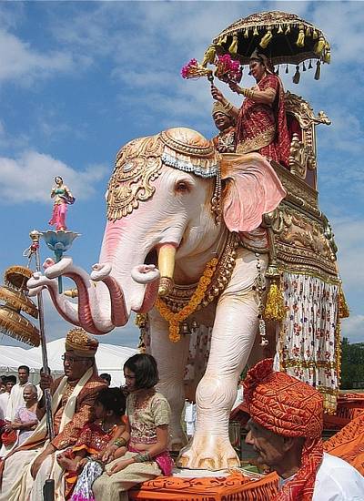 Riding on an 'elephant', lay donors lead the procession of the idol before an abhiṣeka – anointing ceremony. A husband and wife play the parts of king and queen, accompanied by symbols of high rank, such as crowns, parasol and heavily decorated elephant.