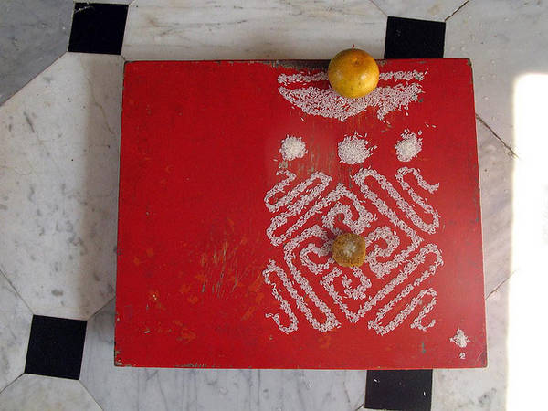The nandyāvarta below three circles symbolising the three jewels of Jainism while the crescent at the top represents the siddha-śilā. The fruits represent souls at various stages while the auspicious symbols are in rice. Such offerings are common.