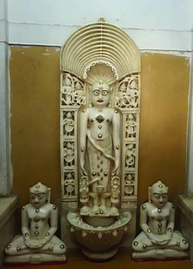 Temple image of the 23rd Jina, Pārśva, and his attendants Dharaṇendra and Padmāvatī on each side of his legs, who form part of the entourage of the Jina image – parikara. The sitting statues either side are not part of his entourage.
