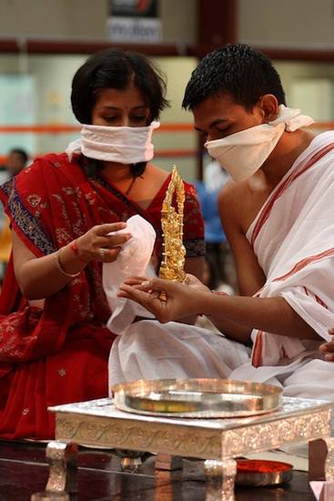 Lay people in Melbourne, Australia, perform the ābhiṣeka – 'anointing ceremony' – of a small figure of the goddess Padmāvatī. The worshippers have covered their noses and mouths so they do not accidentally pollute the statue.